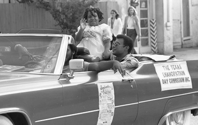 Man and little girl in convertible in parade; banner on side of car says "The Texas Emancipation Day Commission Inc"